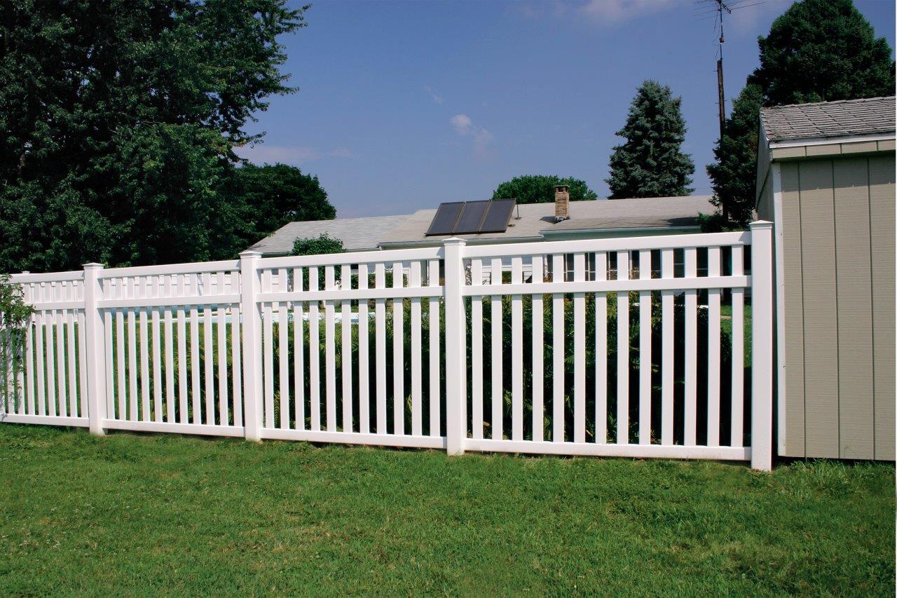 Side view of a white fence surrounding a yard with green grass