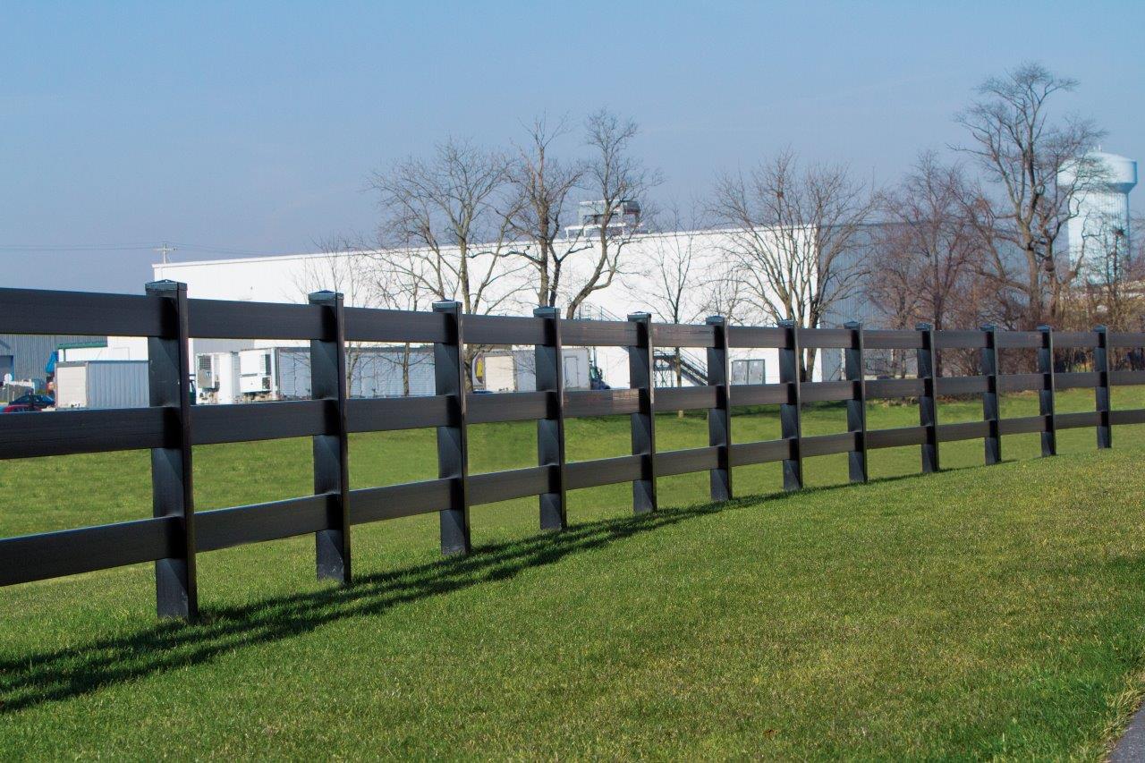 A black rail fence surrounding a large field with green grass, and a large white building in the background