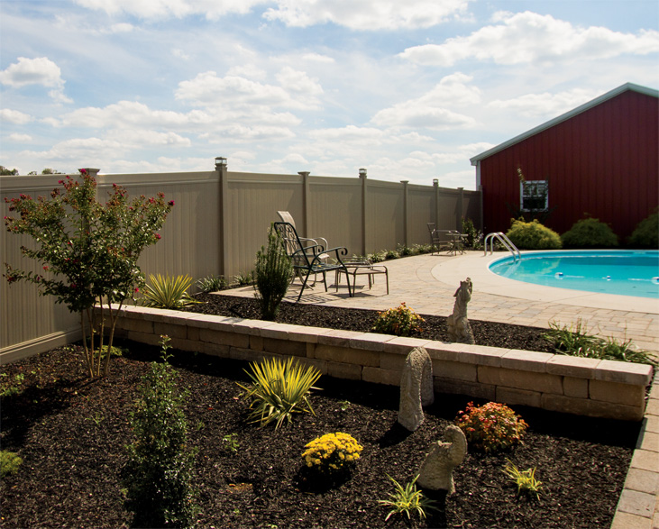 A backyard large backyard with a flower garden, a pool, and a red barn surrounded by a large vinyl fence