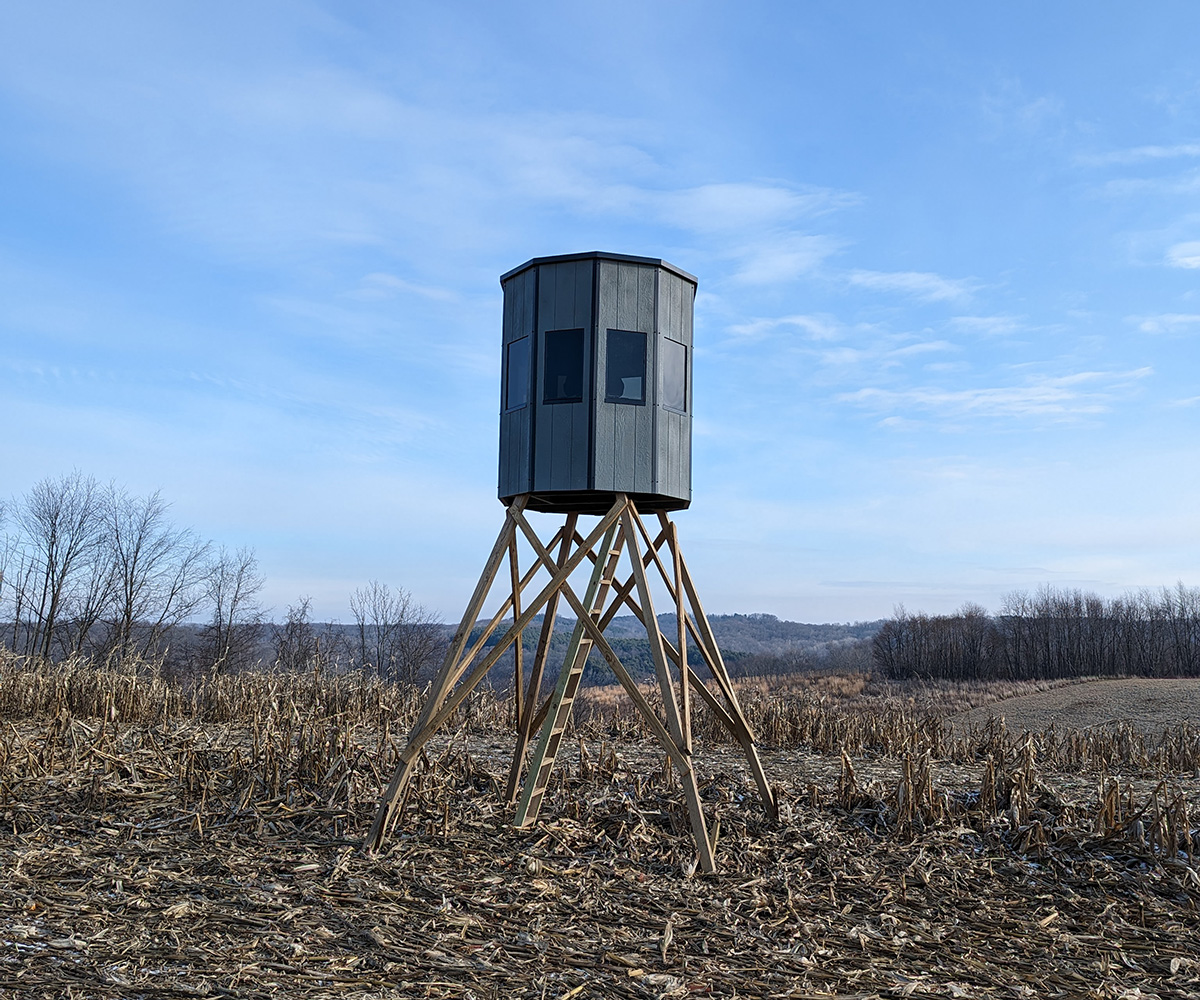 A hunting blind in the middle of an empty field under clear blue sky