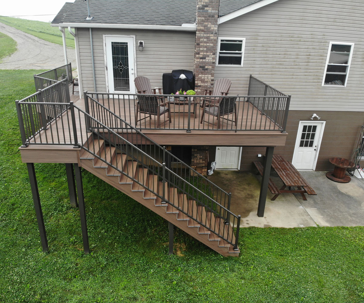 An elevated wooden deck attached to the back of a house featuring sturdy black railing and steps leading to the backyard